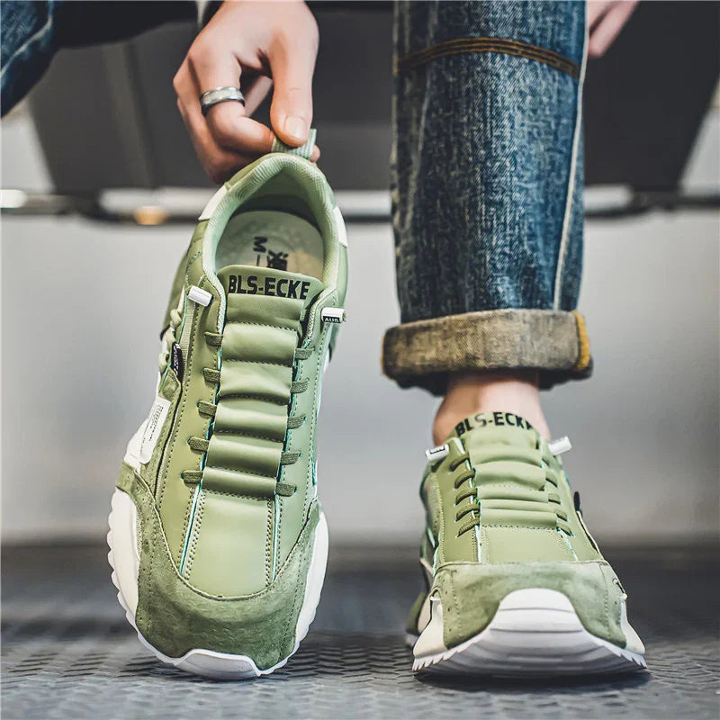 Person wearing and holding green BLS-ECKE sneakers with rolled-up jeans on textured floor