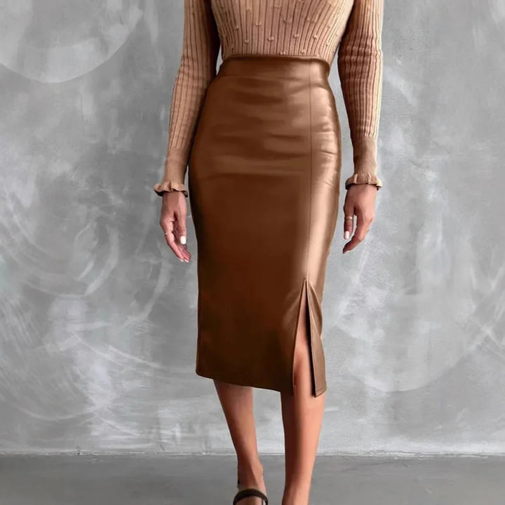Woman wearing a brown faux leather midi pencil skirt with a front slit and a beige ribbed sweater