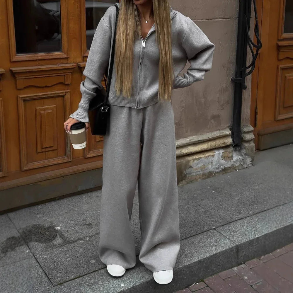 Woman wearing grey zip-up sweater and wide-leg pants holding coffee cup on city street