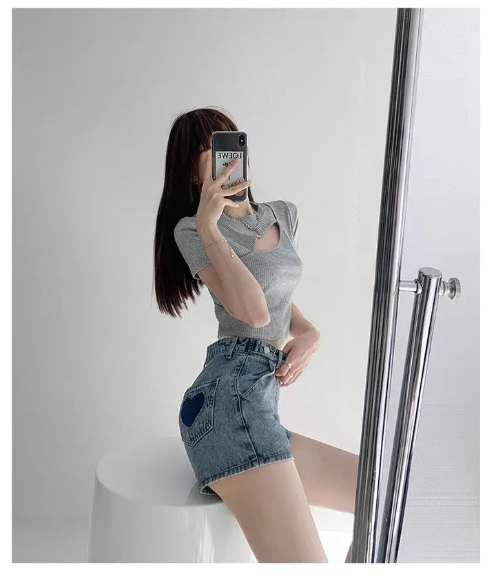 Woman taking mirror selfie wearing grey cutout crop top and denim shorts with heart patch on pocket