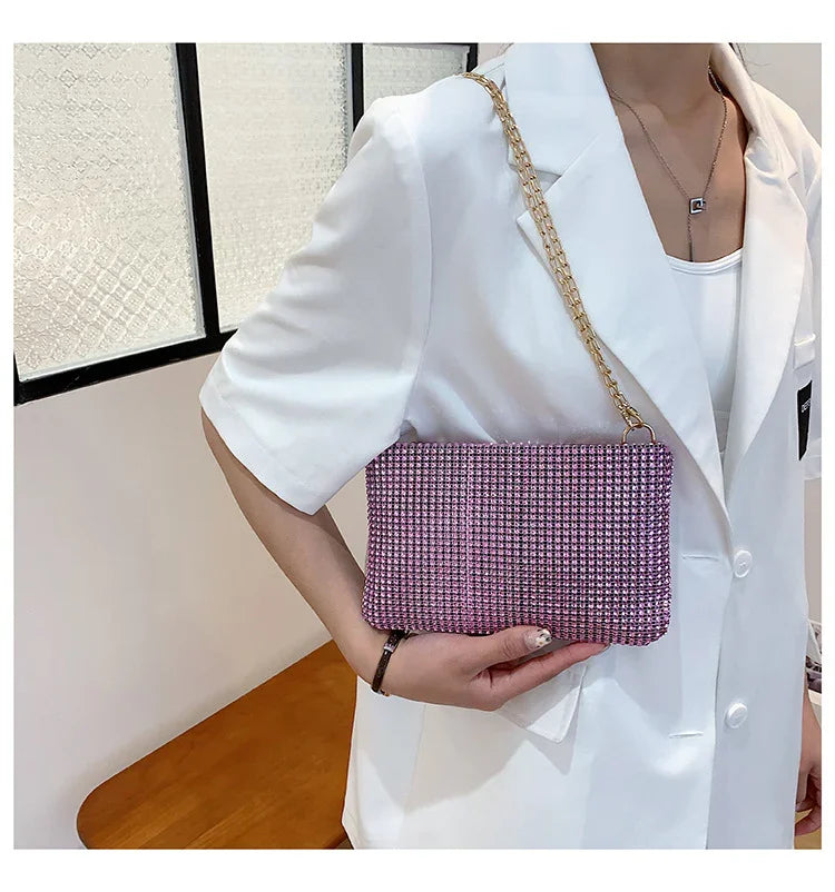 Woman wearing white blazer holding pink rhinestone clutch bag with gold chain strap indoors