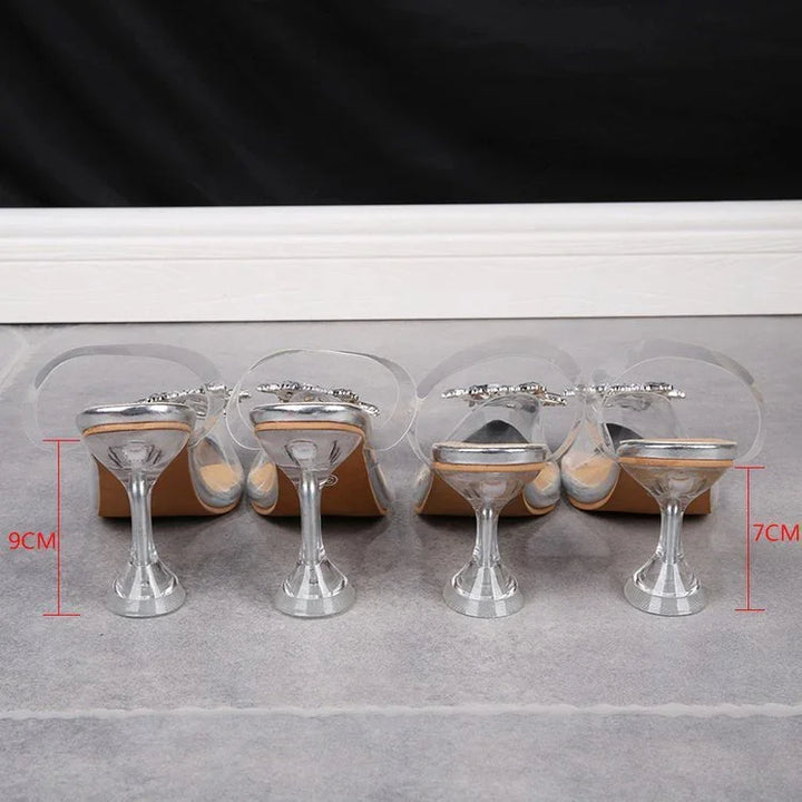 Two pairs of transparent high-heeled sandals with silver heels measuring 9cm and 7cm on grey floor