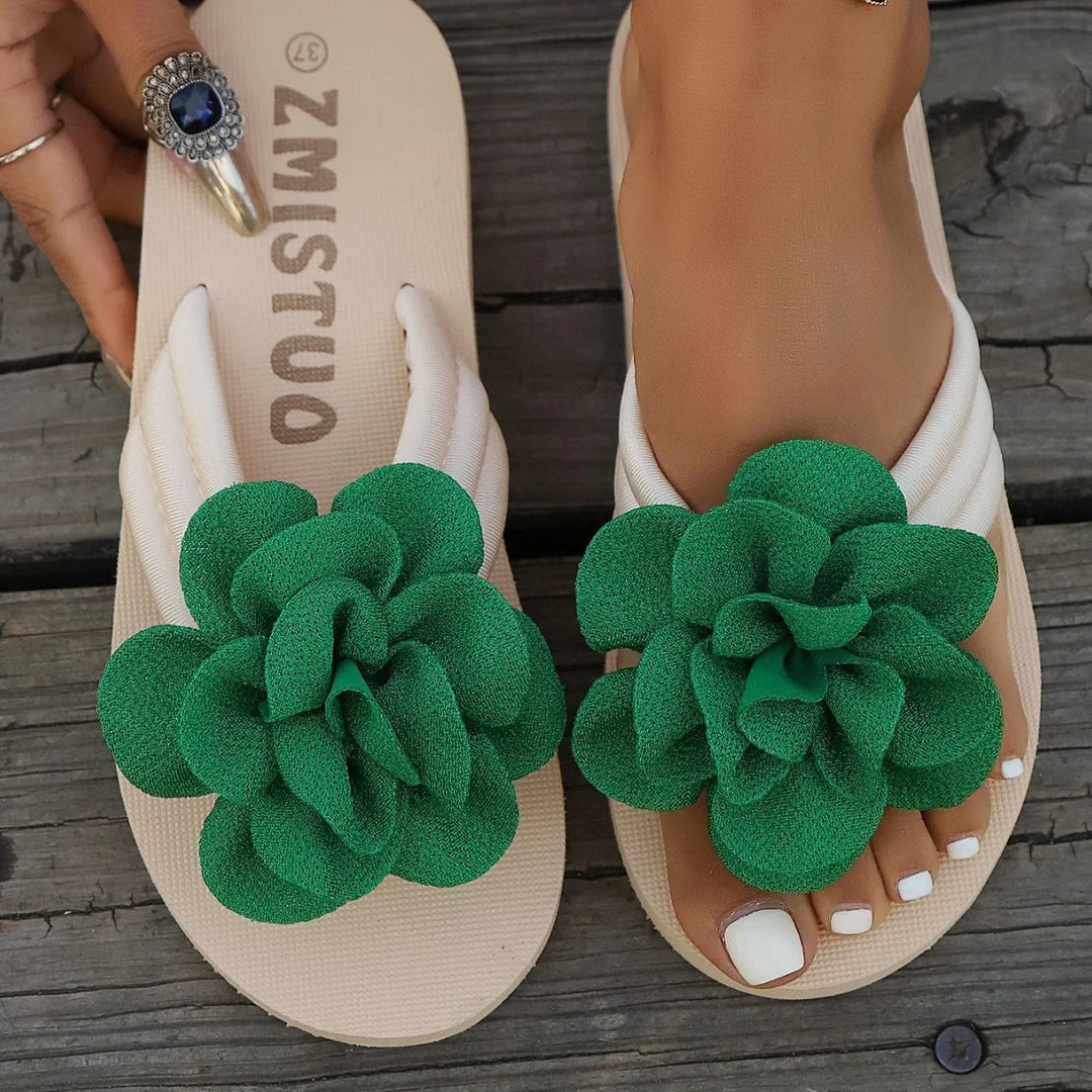 Beige women's sandals with large green fabric flower decoration on wooden background