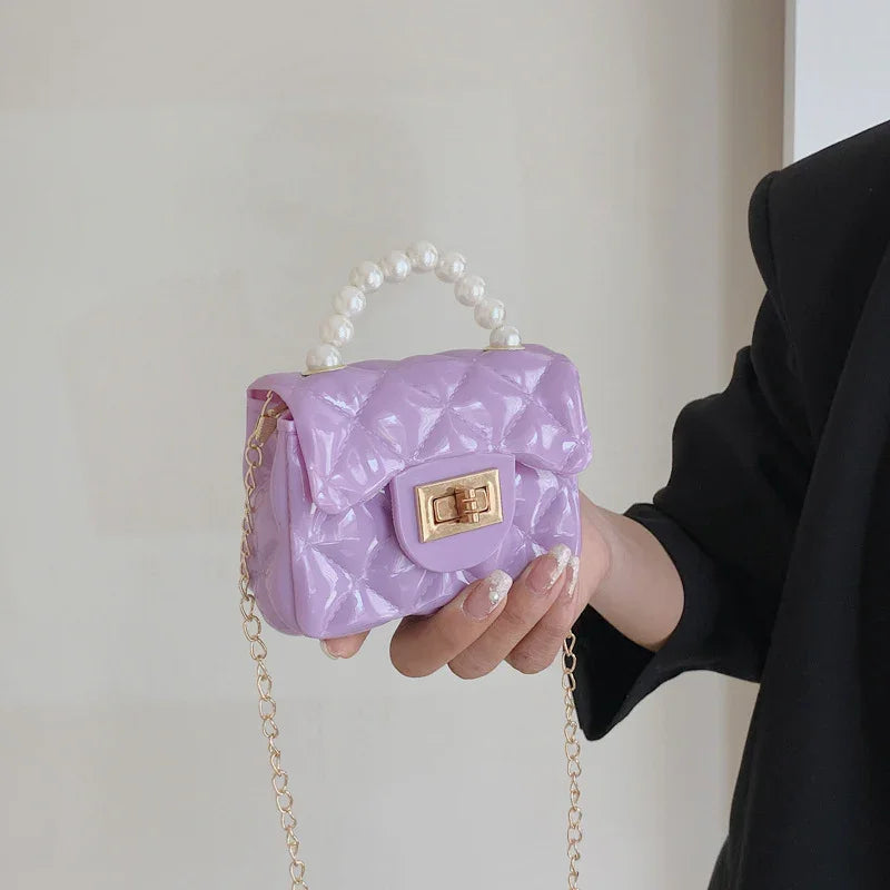 Hand holding a small lavender quilted handbag with pearl handle and gold chain strap