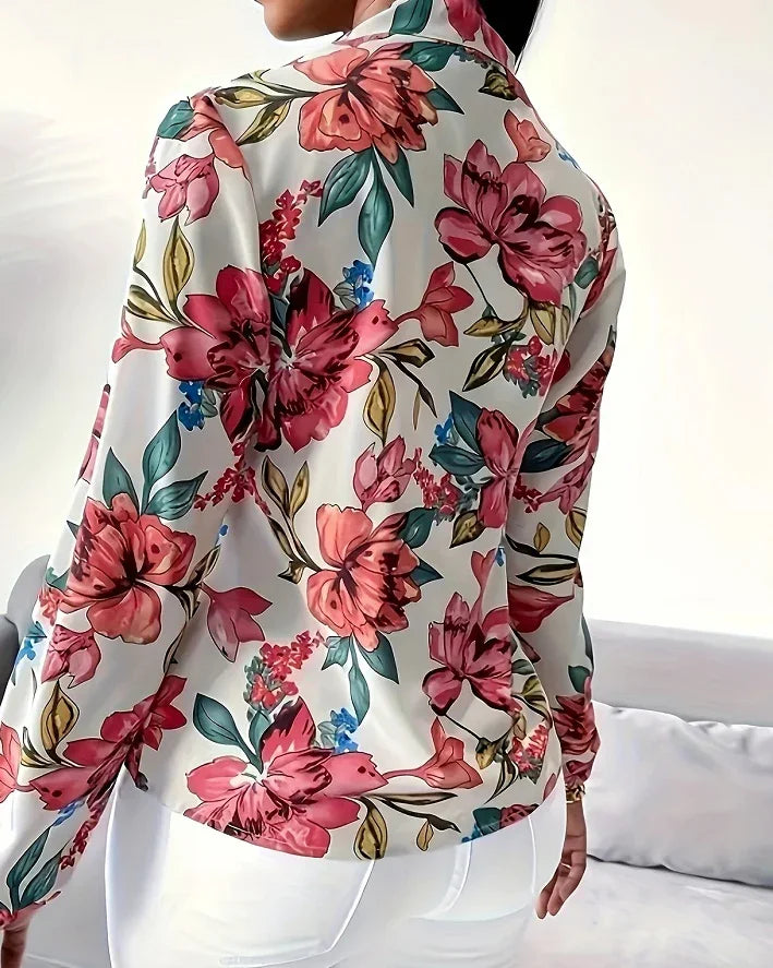 Woman wearing a white floral blouse with large pink and red flowers and green leaves, paired with white pants