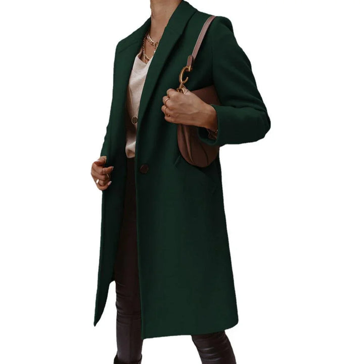 Woman wearing dark green long coat, beige top, black pants, and carrying brown shoulder bag
