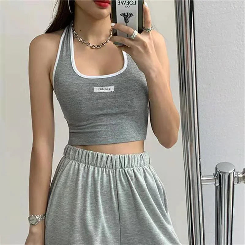 Woman wearing a gray cropped tank top and matching gray sweatpants taking a mirror selfie