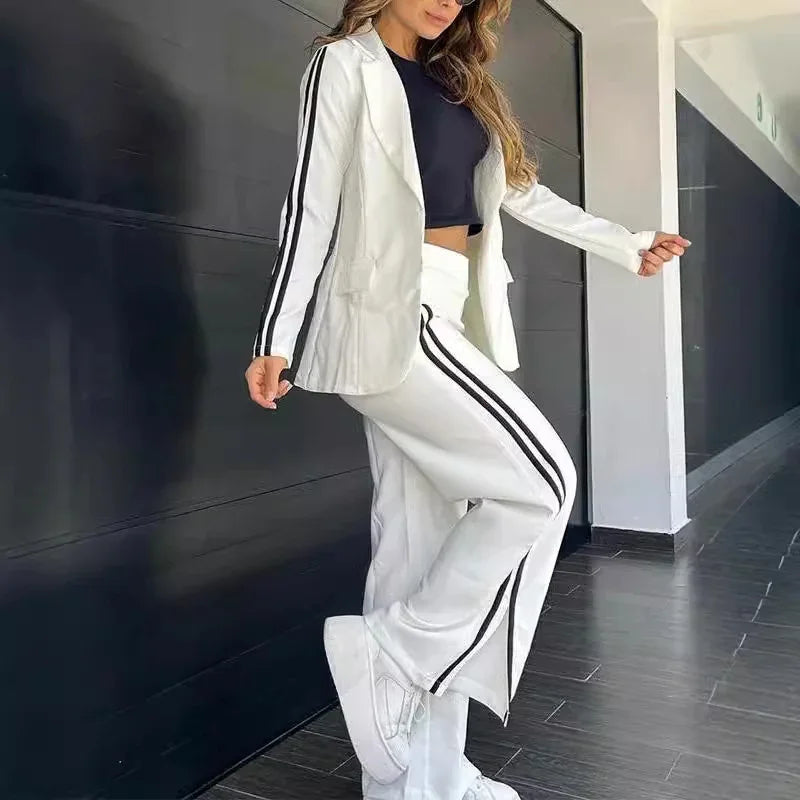 Woman wearing white blazer and pants with black stripes, black crop top, and white platform sneakers indoors