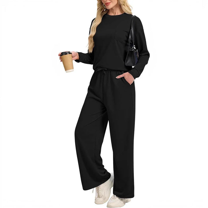 Woman in black long sleeve top and wide-leg pants holding coffee, wearing white sneakers and black handbag