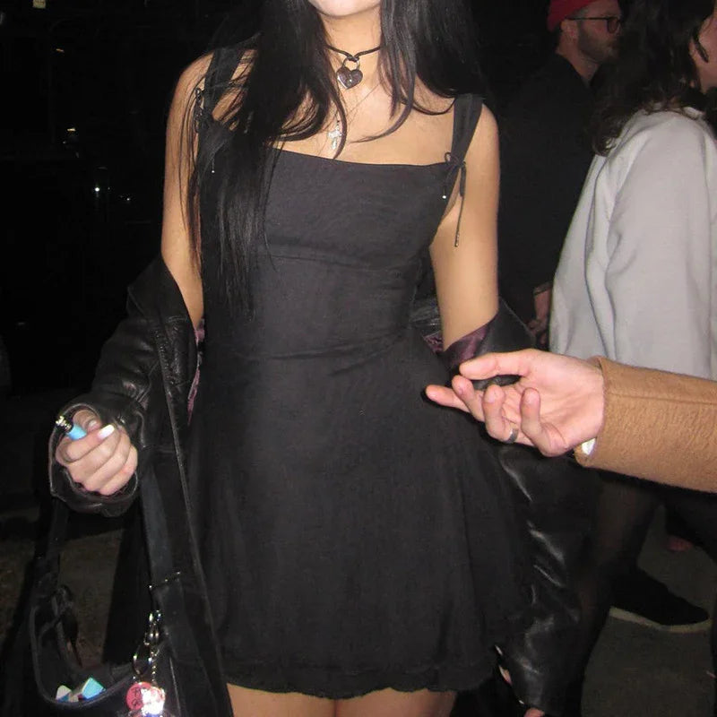 Young woman in black dress and leather jacket holding hands, night setting with people in background