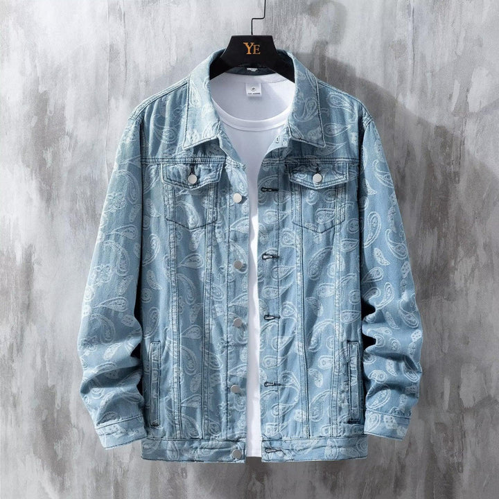 Light blue denim jacket with white paisley pattern over a white t-shirt on black hanger against gray textured wall