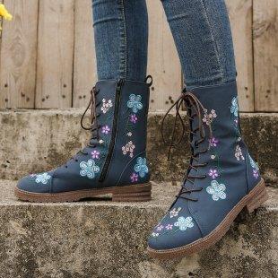 Lace-up navy blue leather boots with colorful floral embroidery worn with blue jeans on concrete steps