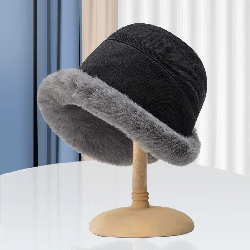 Black winter bucket hat with gray faux fur trim displayed on wooden stand
