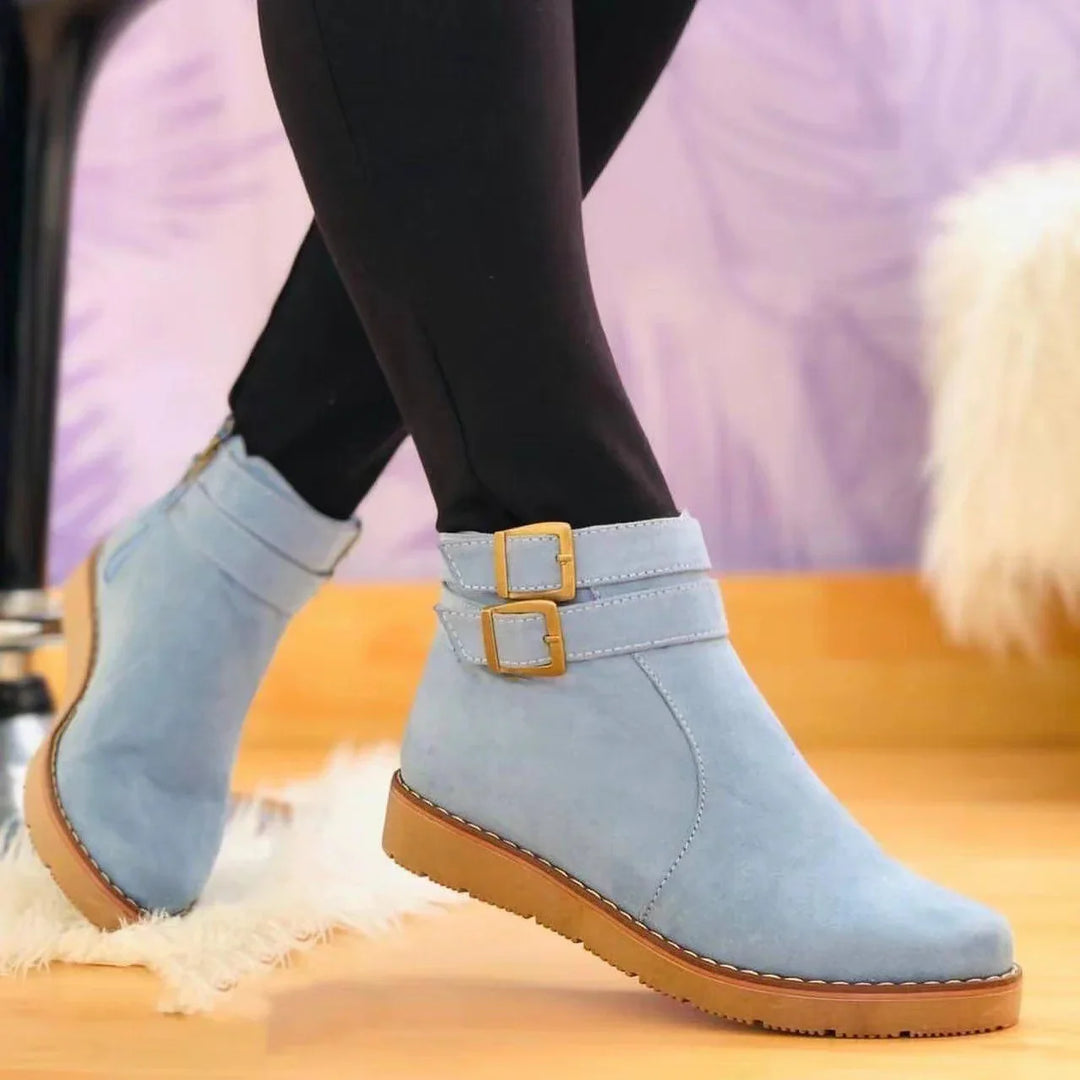 Light blue suede ankle boots with double gold buckles and tan rubber soles worn with black leggings