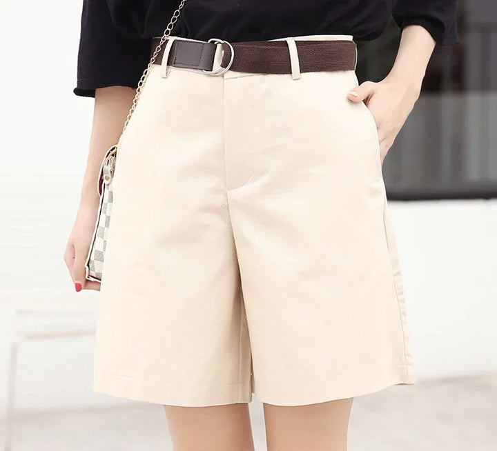 Woman wearing beige high-waisted shorts with a dark brown belt and black top, carrying checkered handbag