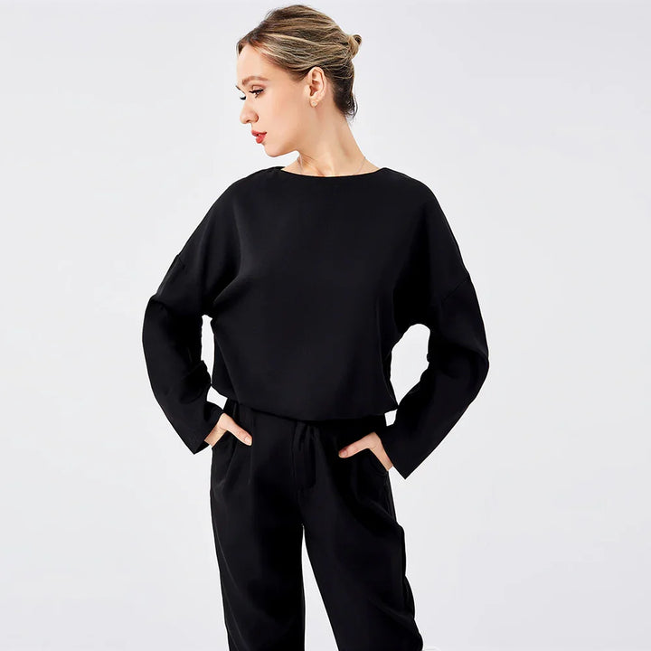 Woman wearing black long-sleeve top and pants posing against white background