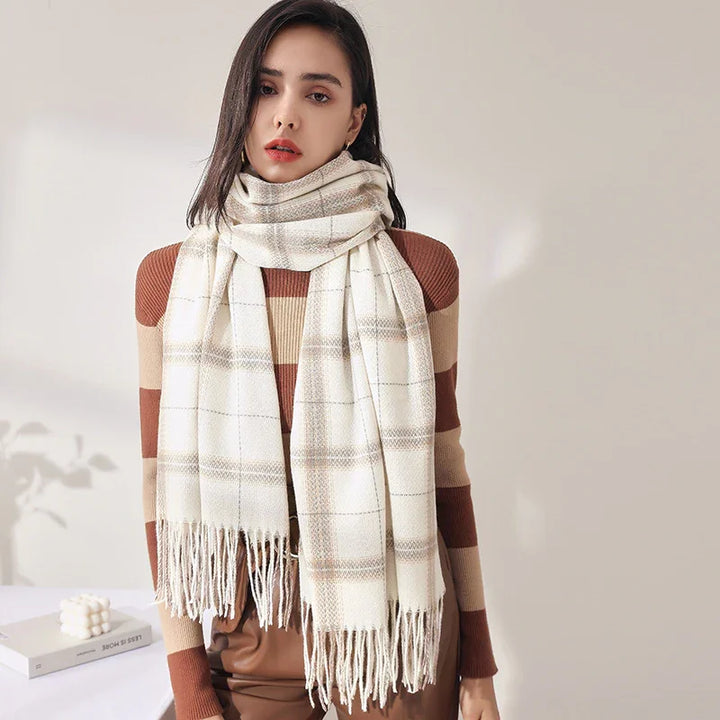 Woman wearing a beige and brown plaid scarf with fringe over a striped brown sweater