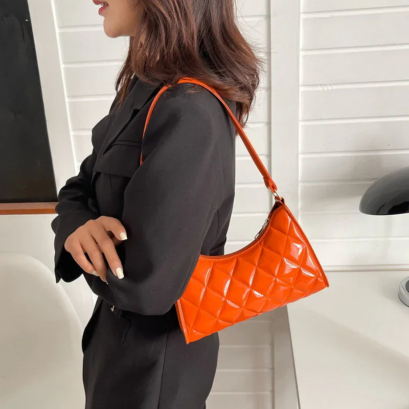Woman in black outfit carrying quilted glossy orange shoulder bag indoors
