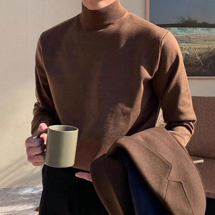 Man wearing brown turtleneck sweater holding matching brown coat and beige ceramic mug