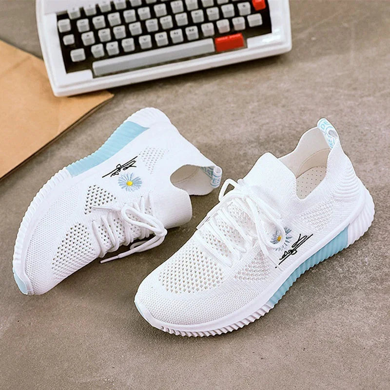 White knitted sneakers with light blue accents and daisy flower embroidery on grey floor