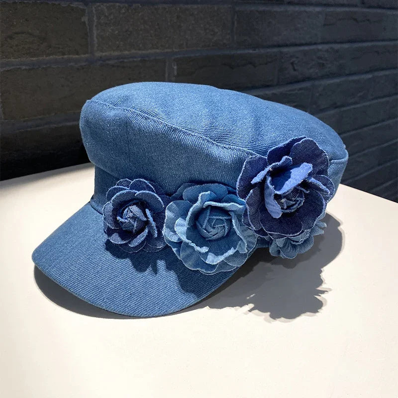 Blue denim hat with a short brim decorated with three denim flower appliques on a white surface