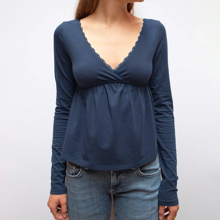 Woman wearing navy blue long sleeve V-neck lace trim top with blue jeans against white background