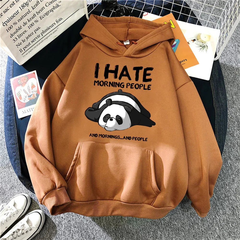 Brown hoodie with cartoon panda and text I hate morning people lying on grey carpet with shoes and tote bag
