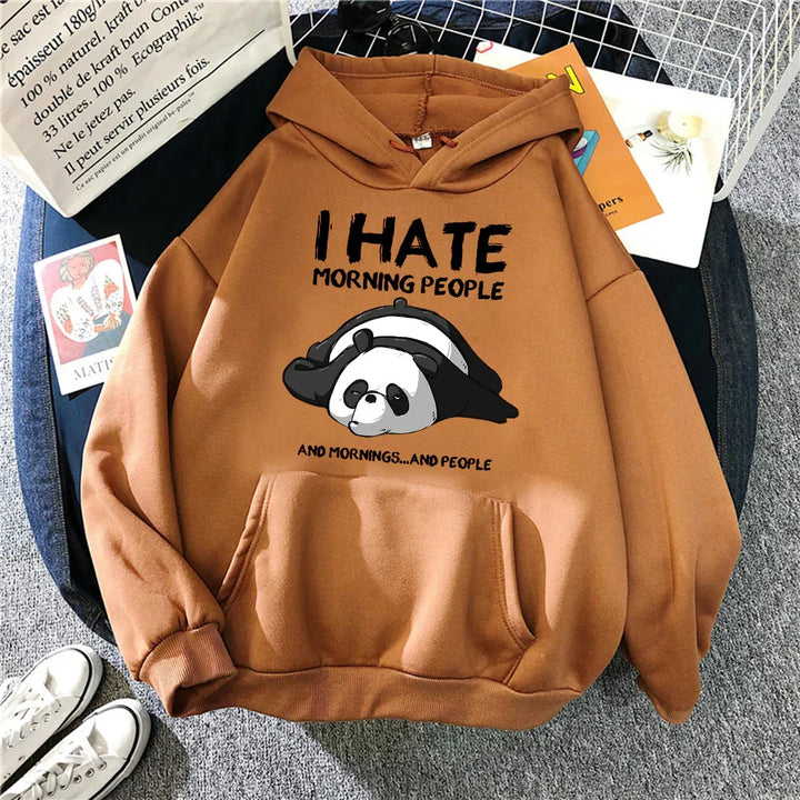 Brown hoodie with cartoon panda and text I hate morning people lying on grey carpet with shoes and tote bag