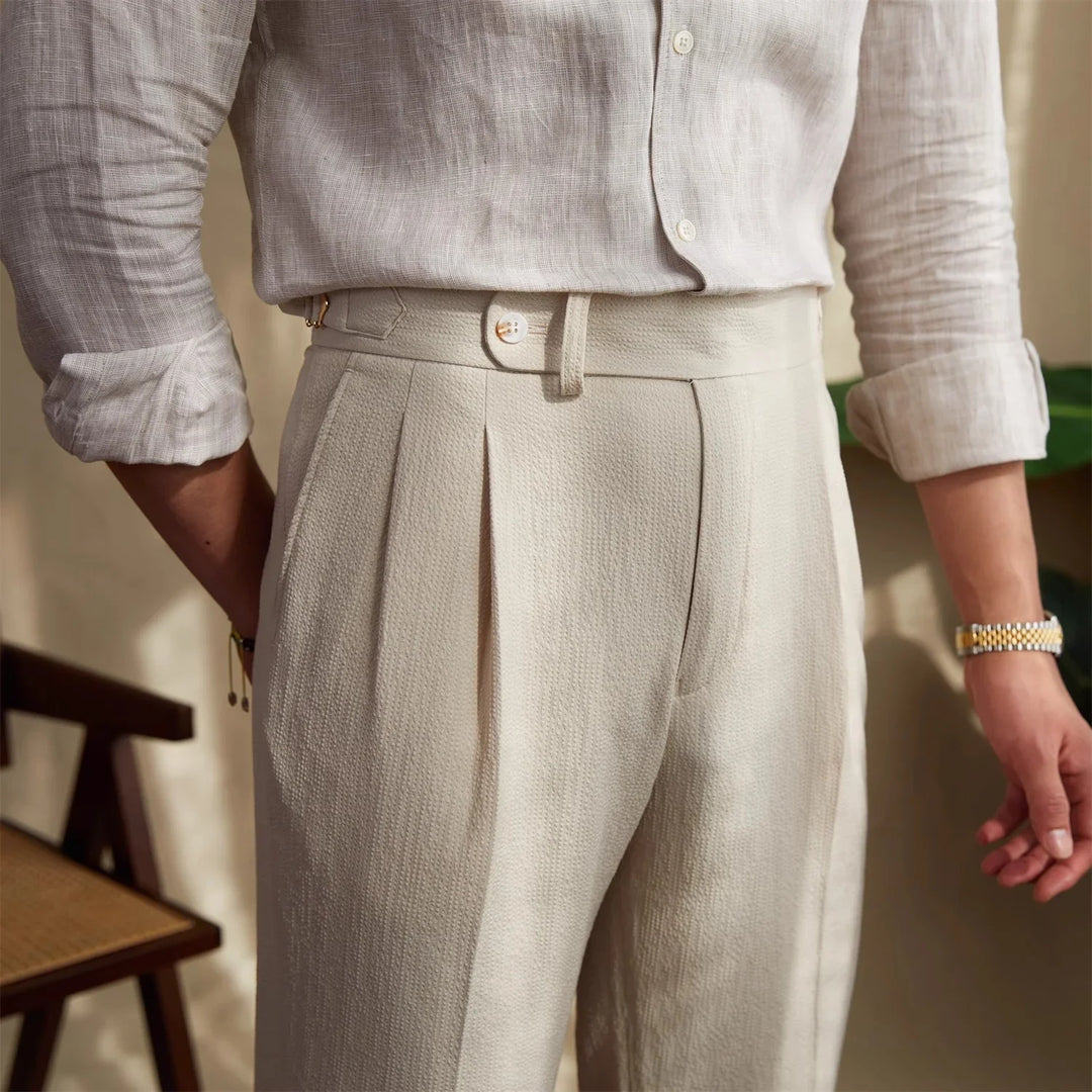 Close-up of man wearing beige textured pleated trousers and rolled-up linen shirt in indoor setting