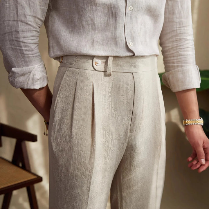 Close-up of man wearing beige textured pleated trousers and rolled-up linen shirt in indoor setting