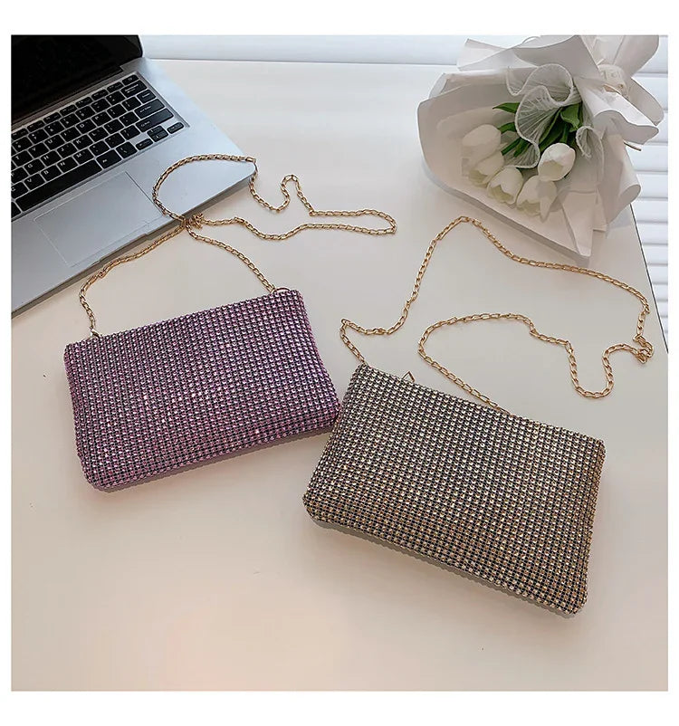 Two sparkling rhinestone clutch bags with gold chain straps on a white surface, beside a laptop and white flower bouquet