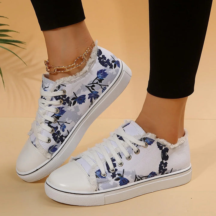 White canvas sneakers with blue floral print and frayed edges worn with black leggings and gold anklet