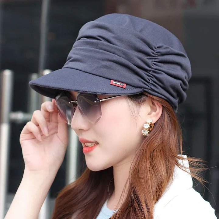 Woman wearing ruched dark blue fashion cap and tinted sunglasses with gold earrings