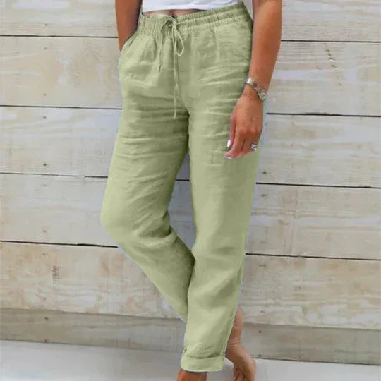 woman wearing light green drawstring linen pants standing barefoot against wooden wall