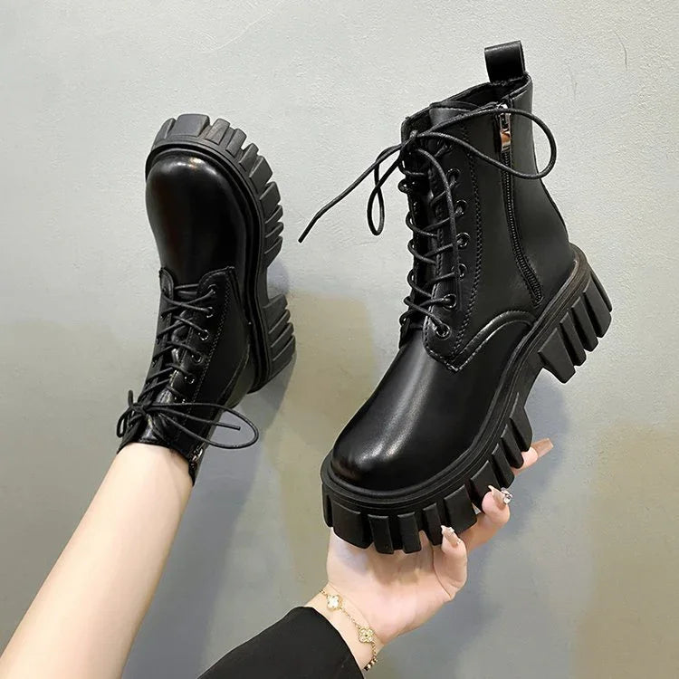 Black chunky platform combat boots with lace-up and side zipper held against gray background