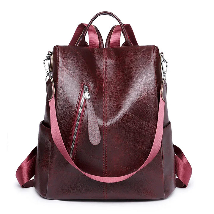 dark red leather backpack with pink shoulder strap, front zipper pocket, and side pockets