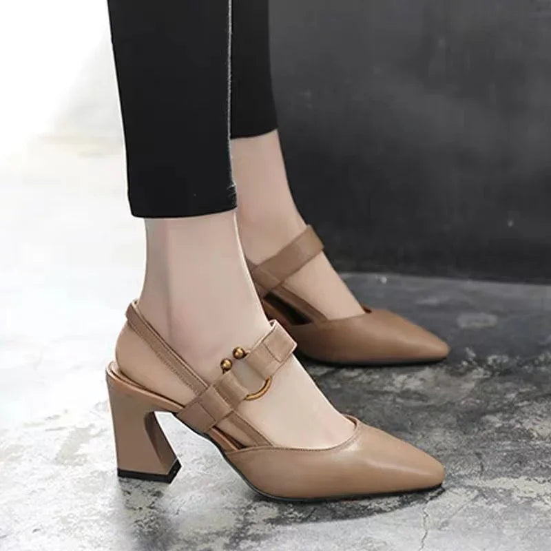 Women wearing beige block heel slingback shoes with strap and gold studs on concrete floor