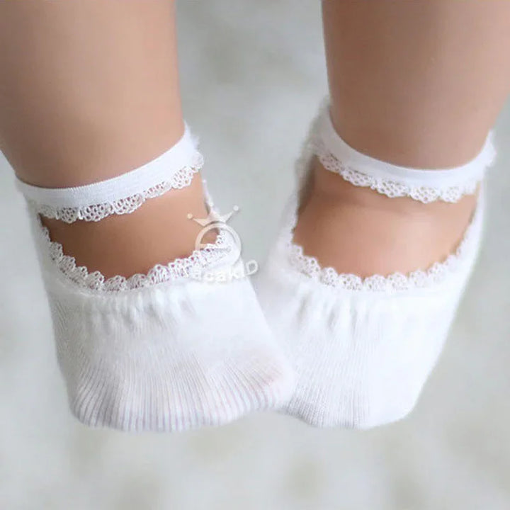 Baby feet wearing white lace-trimmed ankle socks on light background