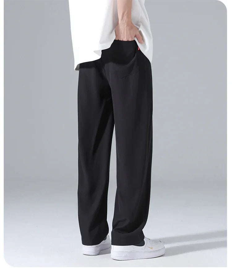 Man wearing loose black pants and white sneakers standing on gray background