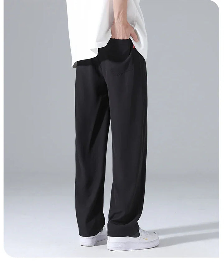 Man wearing loose black pants and white sneakers standing on gray background