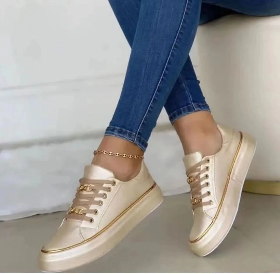 Woman wearing gold satin platform sneakers with chain detail and blue skinny jeans