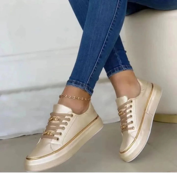 Woman wearing gold satin platform sneakers with chain detail and blue skinny jeans