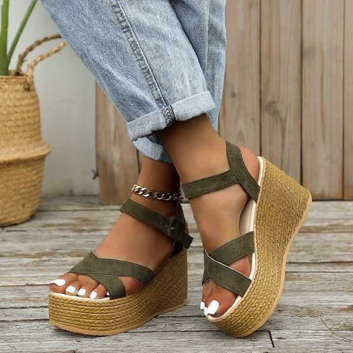 Close-up of feet wearing olive green suede platform wedge sandals with ankle straps and light blue cuffed jeans