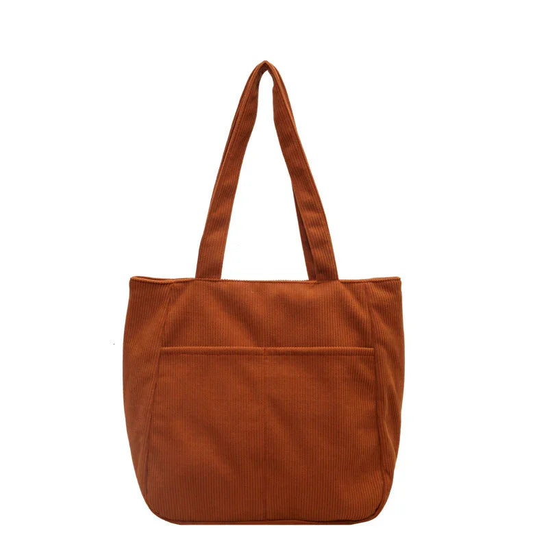 Brown corduroy tote bag with shoulder straps and front pocket on white background