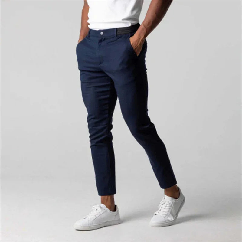 Man wearing slim fit navy blue pants with white sneakers and white t-shirt on gray background