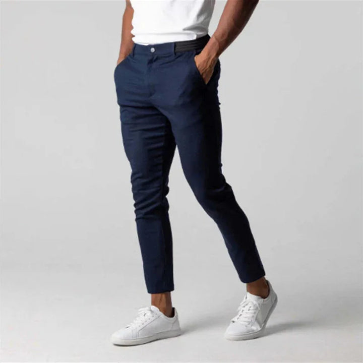 Man wearing slim fit navy blue pants with white sneakers and white t-shirt on gray background
