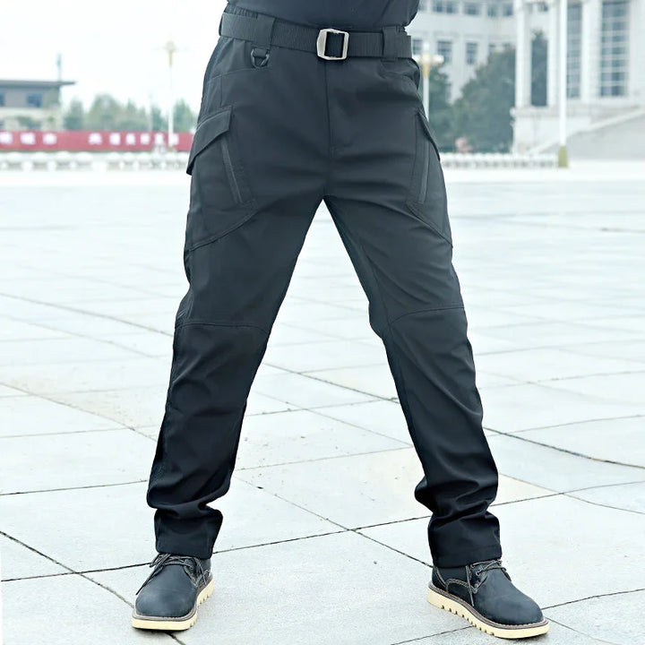 Man wearing black tactical cargo pants with multiple pockets and black boots on city pavement