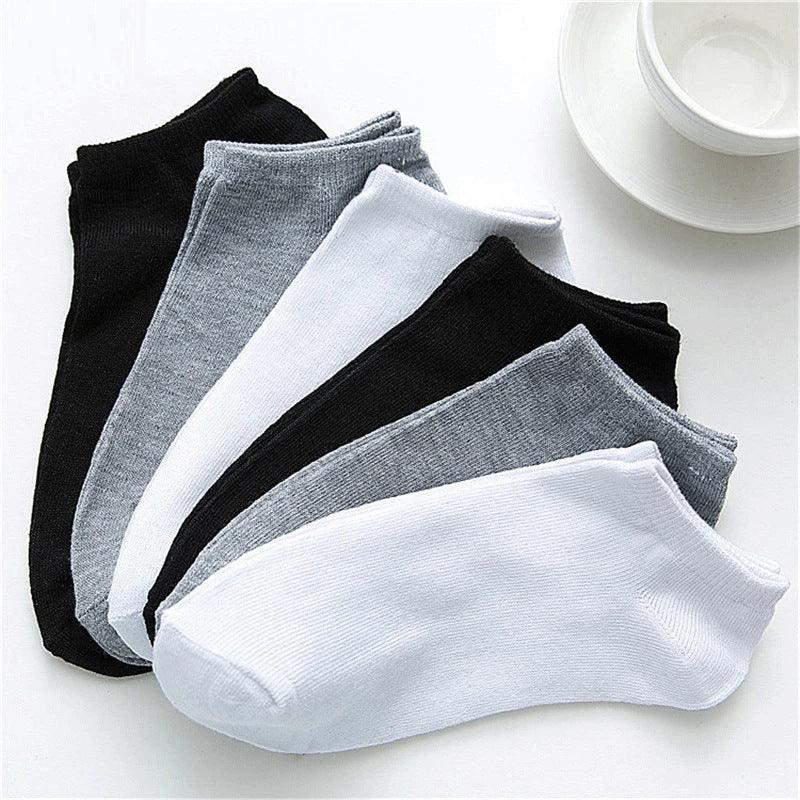 Set of black, grey, and white ankle socks arranged on white surface with white cup and saucer