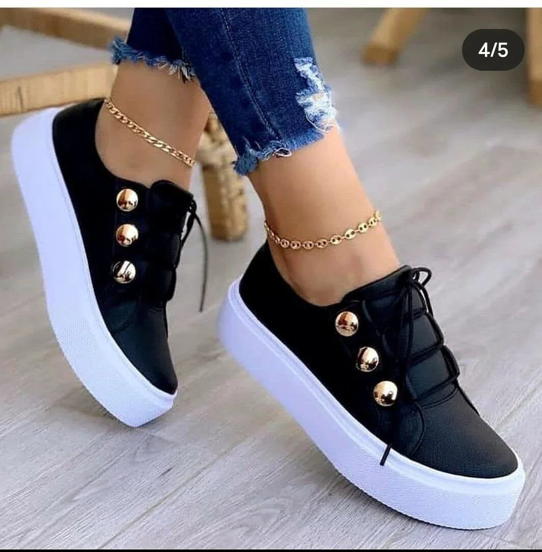 Black platform sneakers with gold buttons and white soles worn with distressed blue jeans and gold anklets
