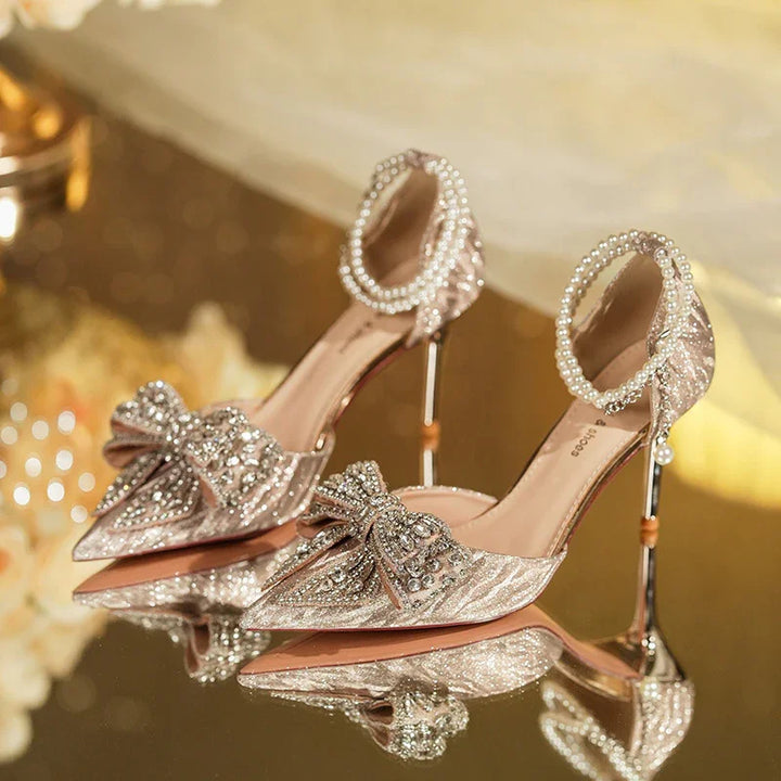 Elegant glittery high heels with crystal bows and pearl ankle straps on reflective surface
